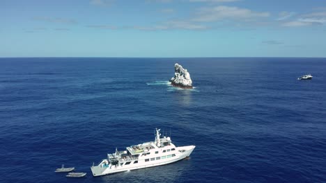 Barco-De-Buceo-Blanco-Cerca-Del-Islote-Rocoso-Roca-Partida-Cubierto-De-Guano-En-El-Pacífico,-Aéreo