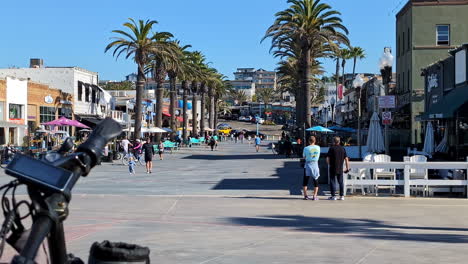 Gente-Caminando-En-El-Paseo-Marítimo-De-Venecia-Con-Palmeras-En-Los-Ángeles,-California,-Estados-Unidos.