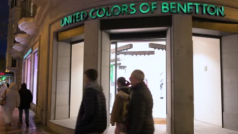 Los-Peatones-Y-Los-Compradores-Pasan-Por-La-Marca-De-Moda-Italiana-United-Colors-Of-Benetton-Store-Durante-La-Noche