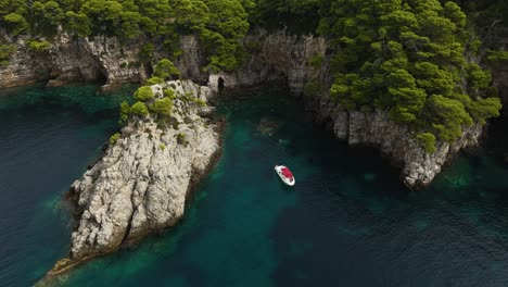 Adriatic-Sea,-Croatia---A-Sailboat-Drifting-Near-the-Steep,-Rugged-Cliffs-of-Kalamota-Island---Aerial-Ascend-Pullback