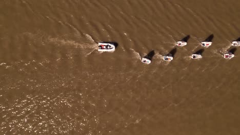 Optimist-sailboats-in-tow-on-the-river---aerial-top-view