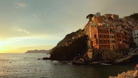 Zeitrafferaufnahme-Des-Sonnenuntergangs-über-Riomaggiore,-Mit-Goldenem-Licht,-Das-Das-Dorf-Vor-Einem-Lebhaften-Himmel-Am-Ruhigen-Meer-Als-Silhouette-Abhebt