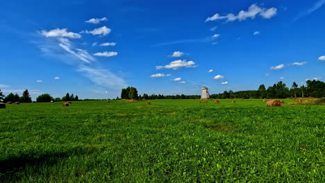 Walk-by-soothing-meadow-covered-in-sunshine,-Latvian-old-windmill-in-the-background