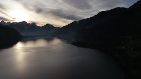 Ein-Blick-Aus-Der-Vogelperspektive-Auf-Walensee,-Churfirsten,-Schweiz,-Während-Die-Sonne-Sanft-Hinter-Schneebedeckten-Berggipfeln-Am-Horizont-Untergeht-Und-Den-Bezaubernden-Schweizer-Charme-Einfängt