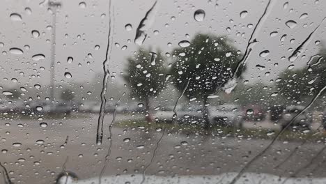 This-is-a-short-video-clip-of-rain,-falling-onto-a-car-window,-creating-large-droplets-and-small-streams-of-water,-flowing-down-the-window