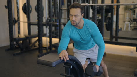 A-Man-In-Blue-Shirt-Is-Doing-One-Arm-Dumbbell-Row-Exercise,-Working-Out-Most-Of-The-Back-Muscles