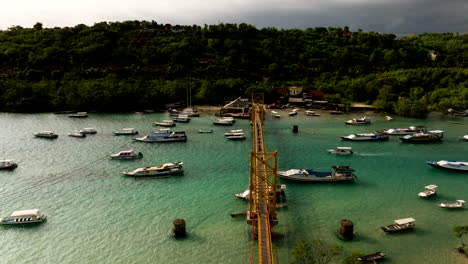 Famoso-Puente-Amarillo-En-Indonesia-Que-Conecta-Las-Islas-Nusa-Lembongan-Y-Nusa-Ceningan-En-Bali-Con-Barcos-Flotando-En-Aguas-Turquesas-Del-Océano