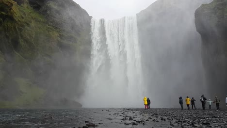 Touristen-Unter-Dem-Skogafoss-Wasserfall-An-Einem-Regnerischen-Frühlingstag,-Wahrzeichen-Islands