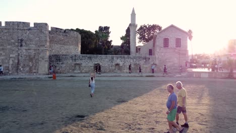 Traveler-Woman-Walking-to-Larnaca-Medieval-Fort,-Cyprus,-Scenic-Orbital-Video