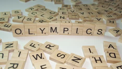 Hand-adds-S-to-Scrabble-tile-letters-on-desktop-forming-word-OLYMPICS