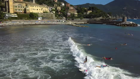 Surfers-riding-waves-on-the-coast-of-Recco-city,-Liguria,-Italy---Aerial-view