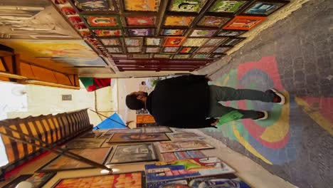 Vertical,-Turistas-Admirando-Las-Obras-De-Arte-Expuestas-En-Las-Paredes-Del-Colorido-Callejón-En-El-Zoco-De-La-Medina-De-Fez,-Marruecos