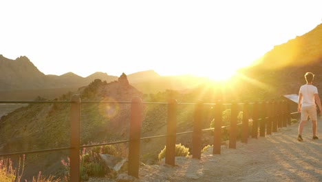 Sun-rays-shining-over-mountains,-view-from-the-tourist-trail-with-guy-in-white-shirt