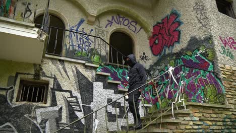 Young-man-in-black-walking-down-the-stairs-of-abandoned-building,-exterior-view