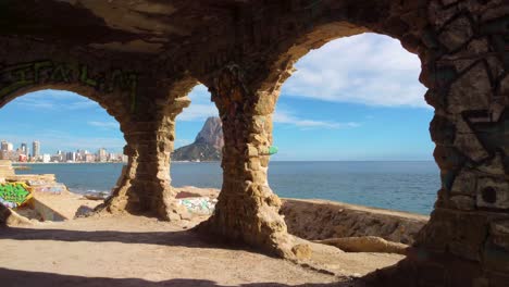 Peñon-d'Ifach---also-known-as-Calpe-Rock:-Dramatic-FPV-Drone-View-of-Calpe-Spains-Iconic-Mountain-and-Coastline-Through-Graffitied-Circular-Windows-in-an-abandoned-graffiti-building