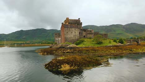 Low-Aerial-Sweep-of-Scottish-Castle,-Eilean-Donan,-on-Loch-Duich-in-the-Scottish-Highlands,-Scotland,-United-Kingdom