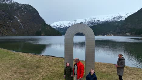 Father-jumps-through-portal-statue-in-slow-motion-as-tourist-family-playing-on-their-trip,-descending-with-fjord-background
