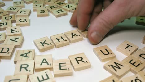 La-Mano-Masculina-Con-Letras-De-Mosaicos-De-Scrabble-Hace-La-Palabra-Khat-En-La-Mesa