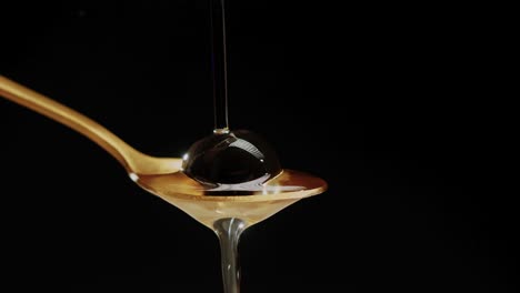 Oil-pours-down-onto-a-spoon-cradling-a-black-olive,-set-against-a-black-background,-representing-the-fusion-of-flavors-and-culinary-artistry