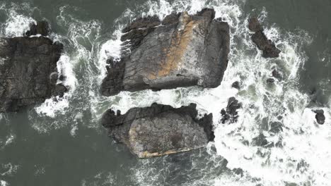 Top-view-aerial-of-the-rocky-and-stony-expanse-of-the-Oregon-coast,-USA,-where-water-meets-the-rugged-shore