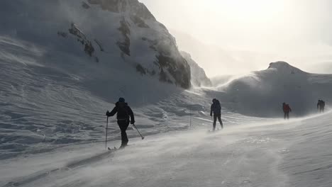 Uphill-view-of-nordic-skiers-skiing-downhill-through-blowing-snow,-Voss,-Norway