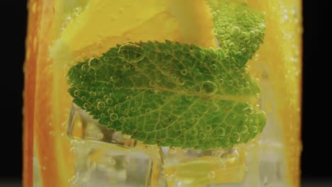 A-close-up-of-lemon-mint-ice-in-orange-lemonade-against-a-black-backdrop