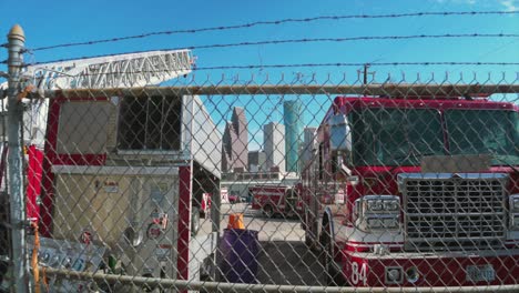 Toma-Alejada-De-Un-Patio-Lleno-De-Camiones-De-Bomberos-Discapacitados-Con-El-Centro-De-Houston-Al-Fondo.