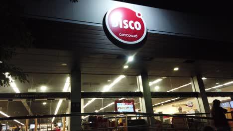 Discoteca-Cadena-De-Supermercados-Entrada-Cartel-Rojo-Logo-Mostrado-Por-La-Noche-La-Gente-Compra-Tienda-En-La-Ciudad-De-Buenos-Aires-Argentina-Noche