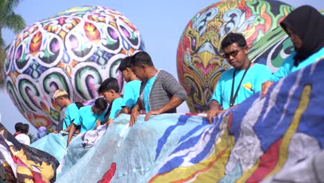 Participants-roll-up-a-hot-air-balloon-that-has-finished-flying-as-part-of-the-hot-air-balloon-festival-in-the-twin-village,-Wonosobo
