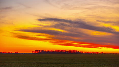 Haze-mist-of-clouds-retreat-above-calm-countryside-fields-with-strong-orange-red-sky