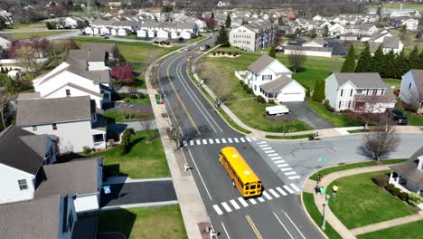 Toma-Aérea-De-Seguimiento-De-Un-Autobús-Escolar-Amarillo-En-Una-Carretera-En-Una-Zona-Residencial-De-Un-Suburbio.