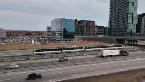 El-Sistema-Automatizado-De-Tren-Ligero-Réseau-Express-Métropolitain-Rem-En-Brossard,-Cerca-De-La-Ciudad-De-Montreal,-El-Tráfico-Por-Carretera-Y-El-Horizonte-En-Un-Edificio-Moderno,-Quebec,-Canadá