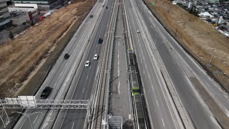 Drone-Siguiendo-El-Sistema-Automatizado-De-Tren-Ligero-Réseau-Express-Métropolitain-Rem-En-Brossard,-Cerca-De-La-Ciudad-De-Montreal,-En-La-Carretera-Principal-Con-Tráfico-De-Vehículos,-Quebec,-Canadá