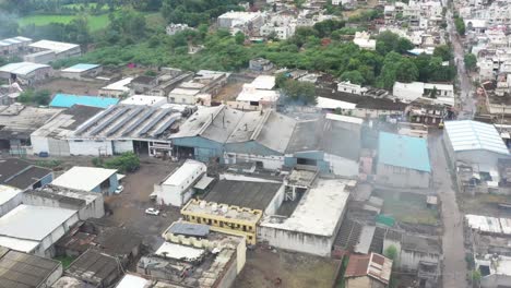 Vista-Aérea-De-Drones-La-Cámara-Del-Drone-Se-Mueve-Hacia-El-Lado-Derecho,-Hay-Grandes-Fábricas-Diferentes,-Se-Ven-Arbustos-Verdes-Y-Campos-Alrededor-De-Las-Fábricas-Y-Las-Casas-También-Son-Visibles