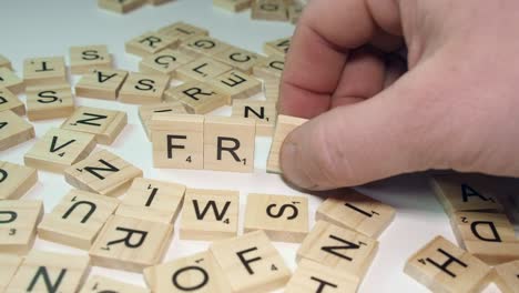 Rechte-Hand-Bildet-Wortbetrug-Aus-Scrabble-Buchstabensteinen-Auf-Weißem-Tisch