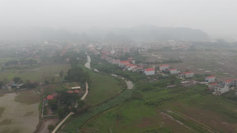 Neblige-Luftaufnahme-Einer-Drohne-Von-Gebäuden-In-Vietnam,-Umgeben-Von-Bäumen-Und-Bergen