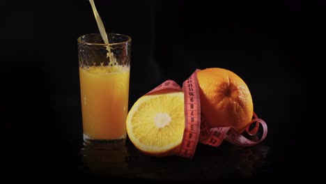 Verter-Jugo-De-Naranja-En-Un-Vaso,-Sobre-Un-Fondo-Negro,-Con-Dos-Naranjas-Cerca,-Simbolizando-La-Esencia-Nutritiva-De-Una-Bebida-Saludable-Y-La-Abundancia-De-Vitaminas-De-La-Fruta.
