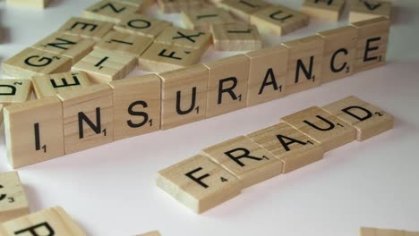 Hand-lays-out-Scrabble-tile-letters-form-words-INSURANCE-and-FRAUD