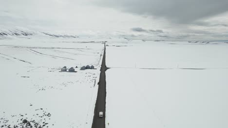 Aerial-view-trails-a-white-camper-van-traversing-a-wintry,-desolate-landscape-in-Idaho,-USA