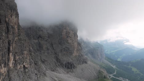 An-aerial-drone-flies-forward,-revealing-the-rugged-peaks-near-Passo-Gardena-covered-in-clouds