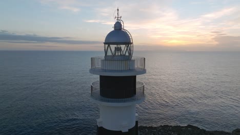Nahaufnahme-Des-Leuchtturms-Cap-D&#39;Artrutx-Auf-Den-Balearen-Auf-Menorca,-Skyline-Im-Hintergrund,-Drohnenluftaufnahme,-Rotierender-Sonnenuntergangshorizont