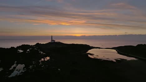 Drohnen-Sonnenuntergangslandschaft-Des-Leuchtturmstrandes-An-Der-Küste-Von-Menorca-über-Dem-Meerwasser-Mit-Farbverlauf,-Farbenfrohe-Skyline-Zur-Goldenen-Stunde