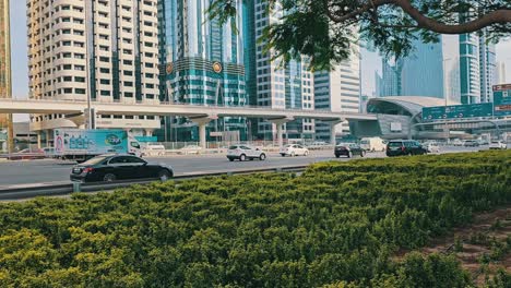 Ongoing-traffic-flow-on-Sheikh-Zayed-Road-in-Dubai,-captured-from-the-green-sidewalk,-symbolizing-a-sustainable-future