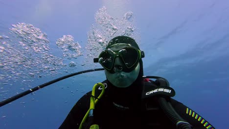 scuba-diver,-clad-in-a-black-and-yellow-Cressi-wetsuit-and-mask,-is-submerged-in-the-clear-blue-waters-of-the-ocean,-with-bubbles-escaping-from-their-regulator