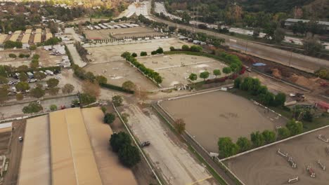 Establishing-Aerial-Shot,-Drone-Looking-Down-at-Los-Angeles-Equestrian-Center-in-Daytime,-Highway-to-the-Right-and-Training-Arenas-Below