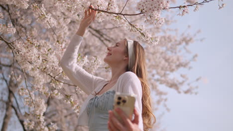 Mujer-Caucásica-Tomándose-Un-Selfie-Con-Flores-De-Cerezo-En-El-Parque-Forestal-Ciudadano-De-Yangjae-En-Seocho,-Seúl,-Corea-Del-Sur