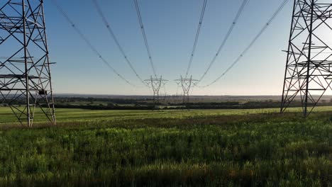 Low-drone-shot-between-massive-powerlines-at-sunset