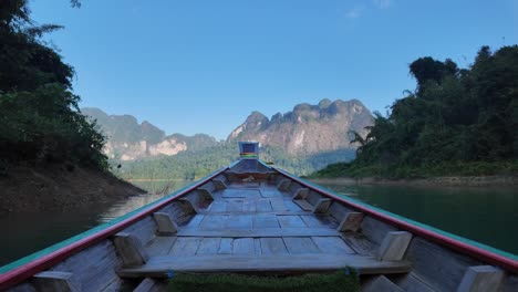 Barco-De-Madera-Tradicional-Navega-Sobre-El-Agua-Entre-Pintorescas-Montañas-Tropicales-En-El-Parque-Nacional-De-Khao-Sok,-Tailandia