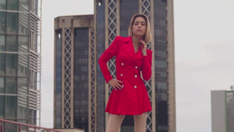 On-a-Port-of-Spain-rooftop,-a-young-Hispanic-girl-in-a-red-dress-contrasts-against-the-backdrop-of-tall-buildings