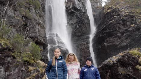 Teenagers-posing-in-front-of-majestic-waterfall-Hesjedalsfossen,-slow-motion